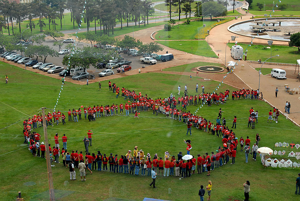 Looking down at a group of people outside on the grass in the shape of the Aids Ribbon