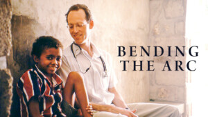 a doctor with a stethoscope around his next sits next to a smiling young boy